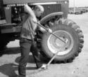 With the wrench bar socket over a tractor wheel lug nut, an adult male (his foot on the support bar) pushes down on the cheater bar to loosen the nut.