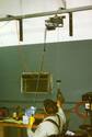 Adult male in a wheelchair pulls the handle attached to a cord that activates the power cable winch, which is rides along the shop elevated roller track.