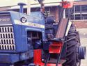 An adult male rides in the seat on the over-the-tire inclined track (attached to the tractorâ€™s rear side frame) that carries him up to the operation station.