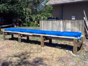 6 blue plastic half-barrels lying open-side-up and end-to-end on a long frame of 4x4 upright posts with horizontal cross beams and a center beam running lengthwise to support the half barrels.